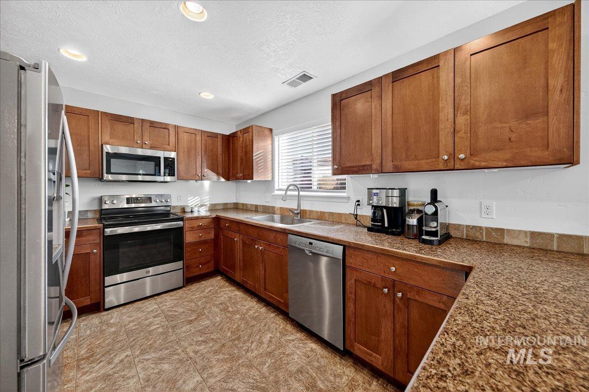 Kitchen featuring appliances with stainless steel finishes, brown cabinetry, recessed lighting, and a textured ceiling