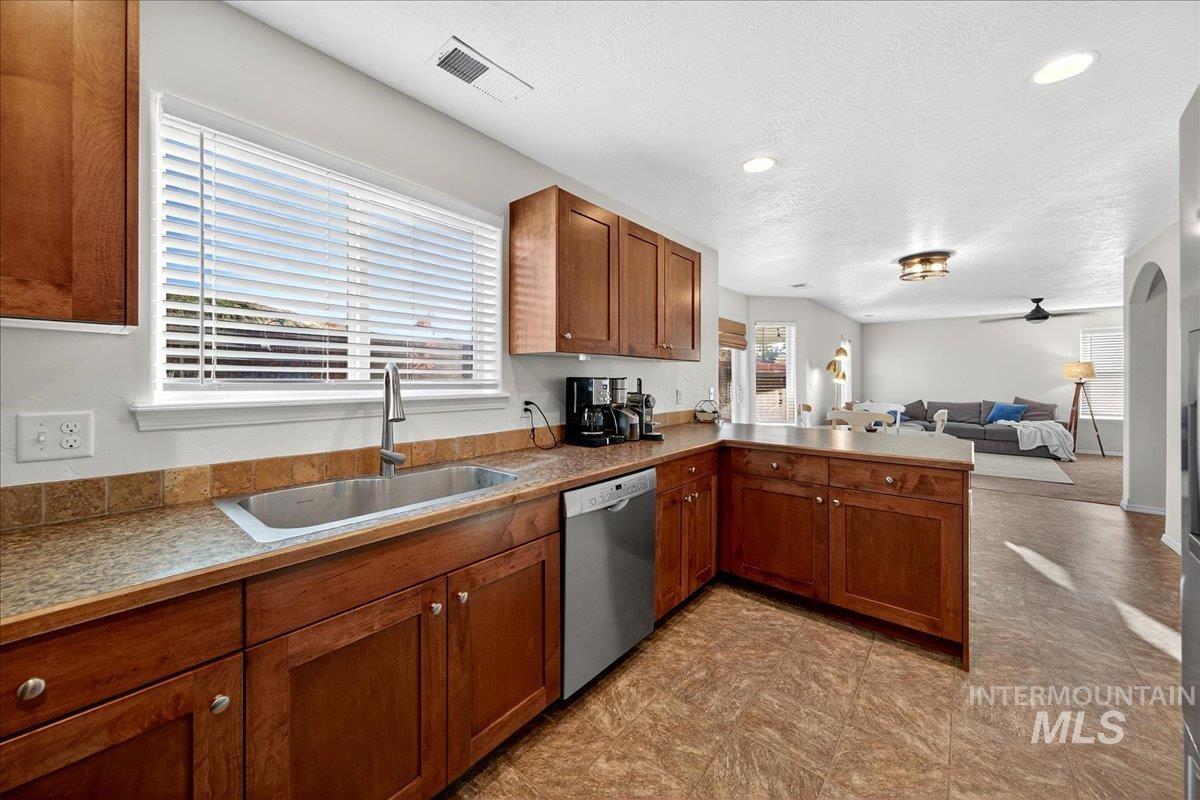 Kitchen with open floor plan, brown cabinetry, a peninsula, stainless steel dishwasher, and a ceiling fan