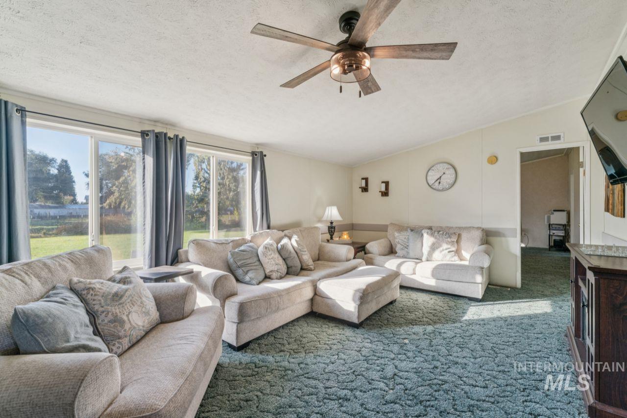 Living room with vaulted ceiling, a textured ceiling, carpet, and ceiling fan