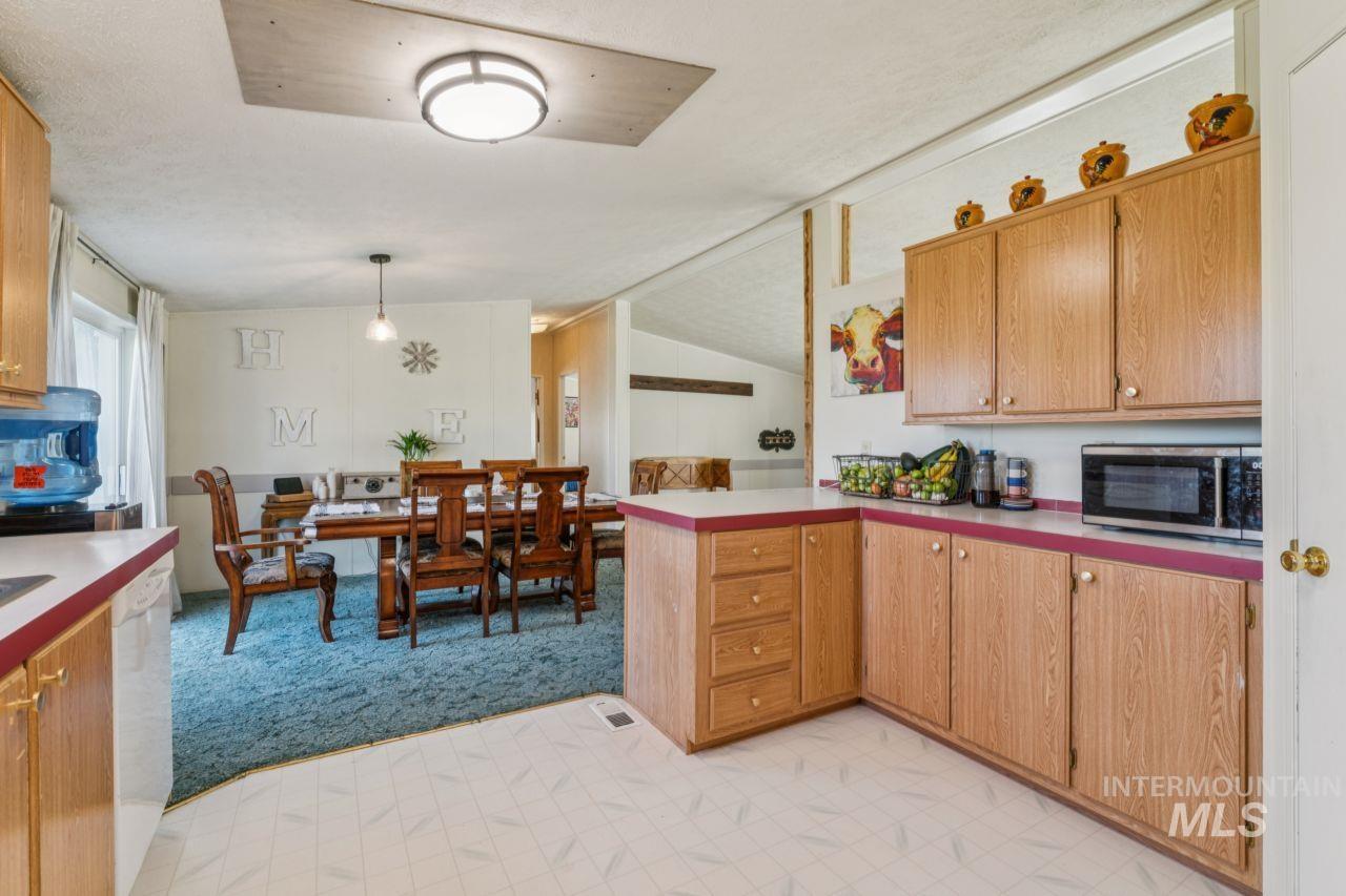 Kitchen featuring a peninsula, light colored carpet, light countertops, vaulted ceiling, and stainless steel microwave