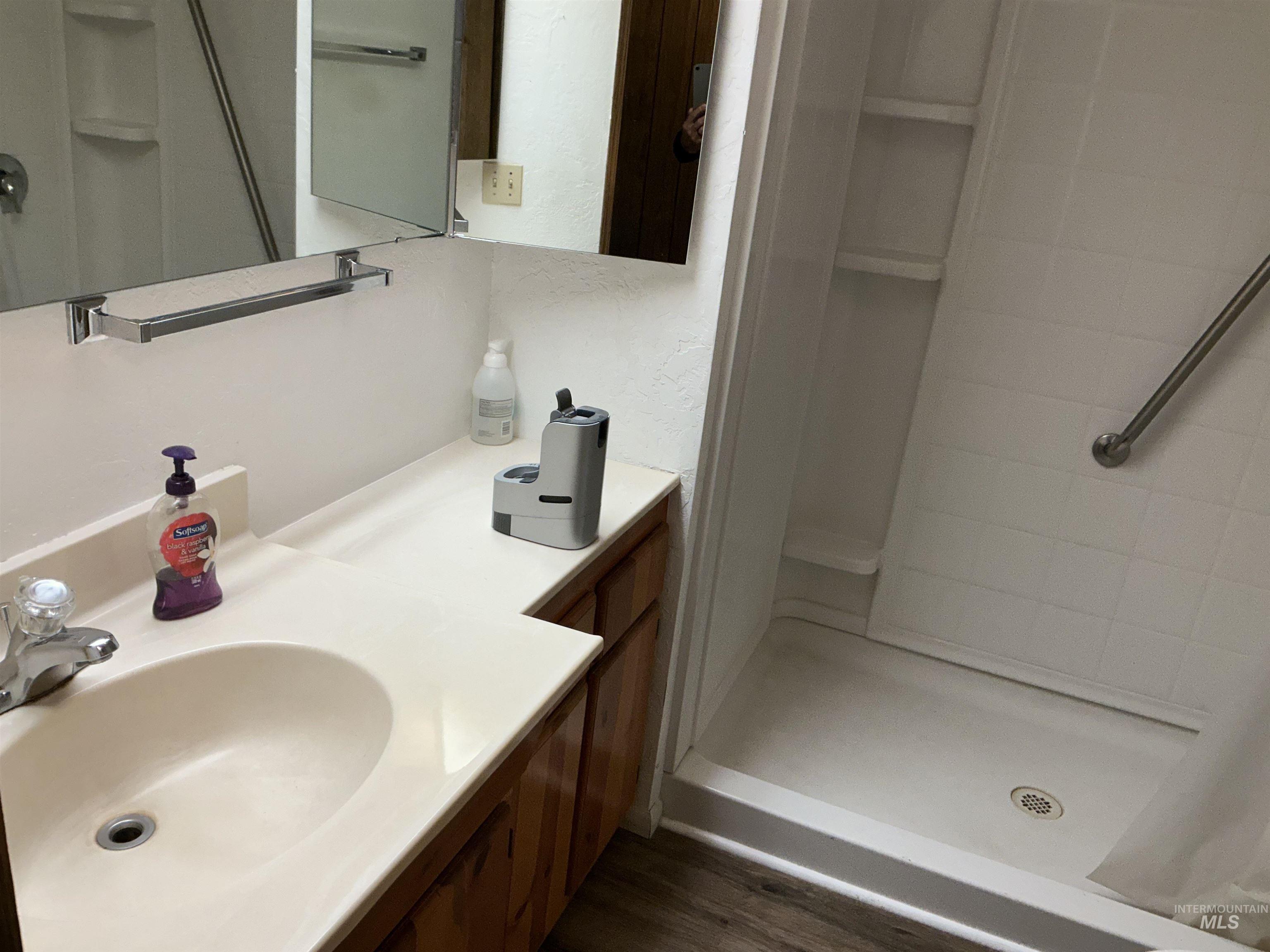 Full bath with a stall shower, vanity, and dark wood-style flooring