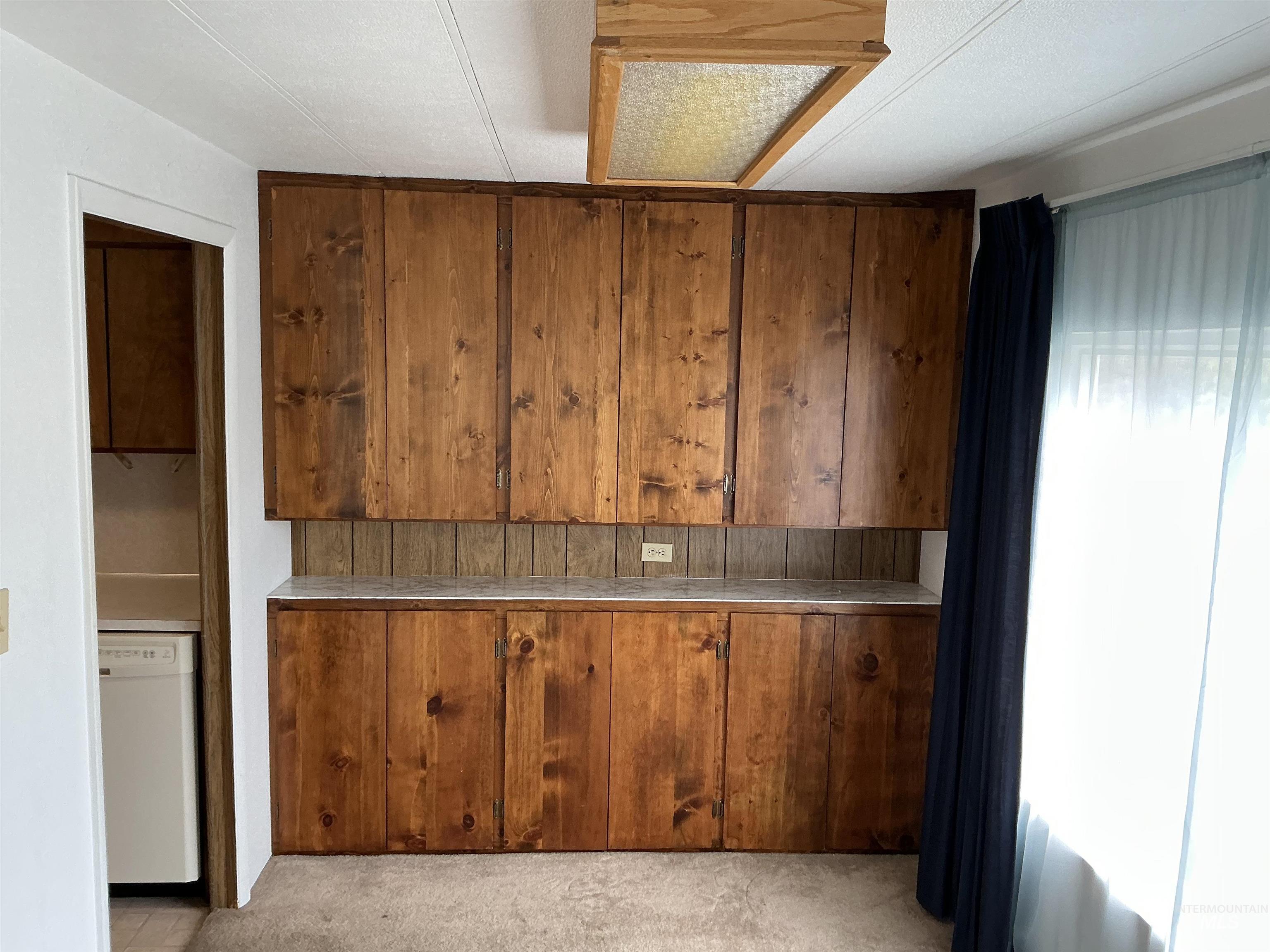 Kitchen with white dishwasher, brown cabinetry, and light carpet