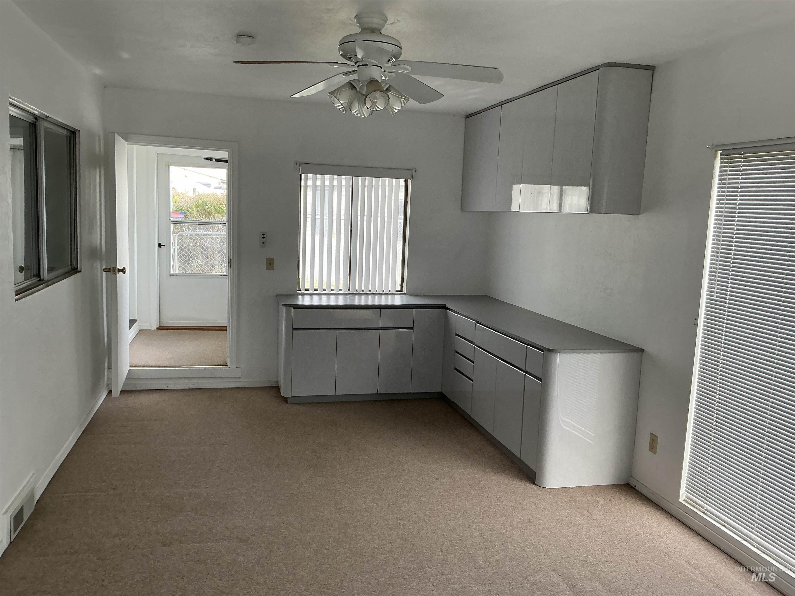 Kitchen with gray cabinetry, a ceiling fan, and light colored carpet