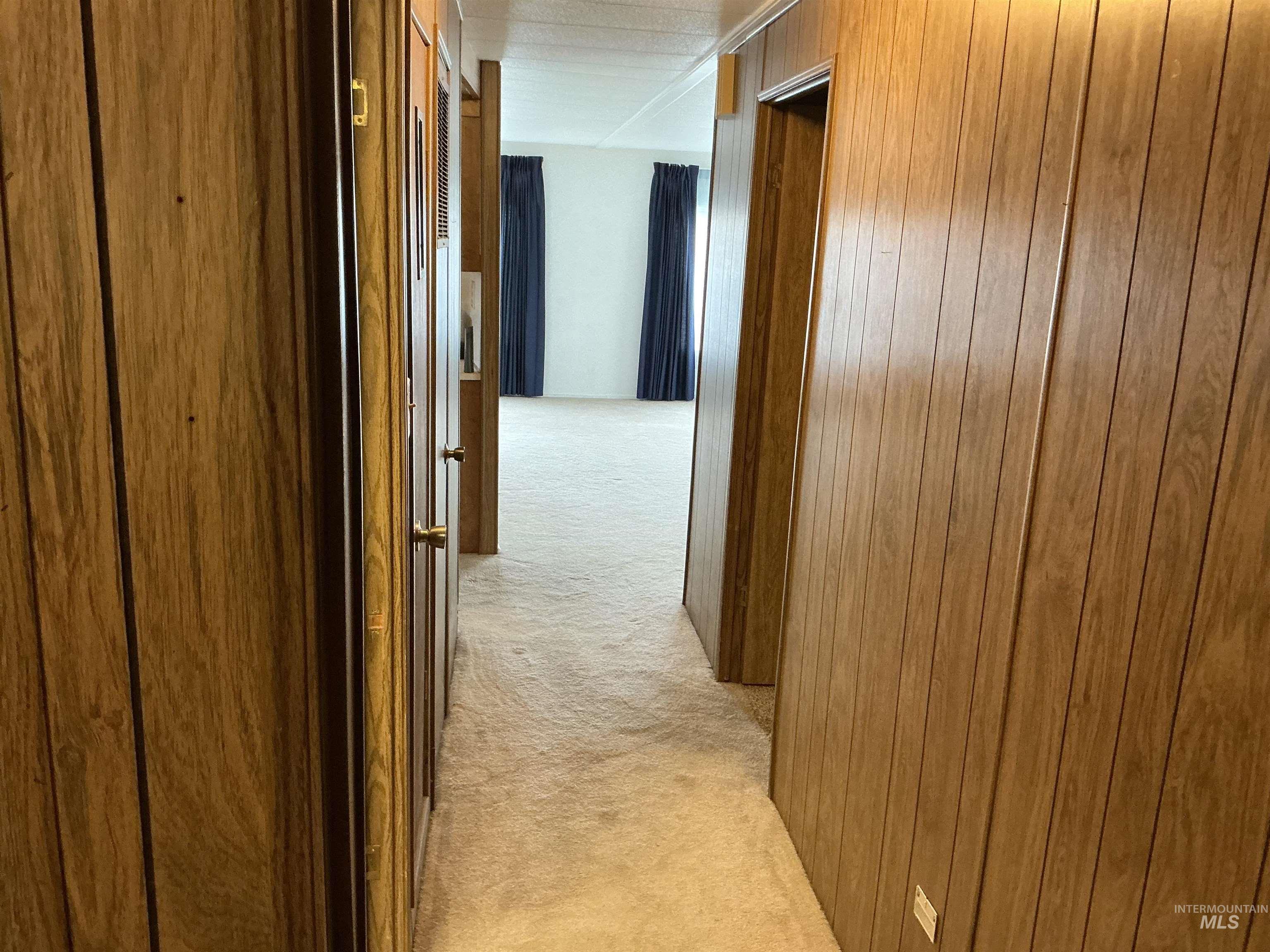 Corridor featuring light colored carpet and wood walls