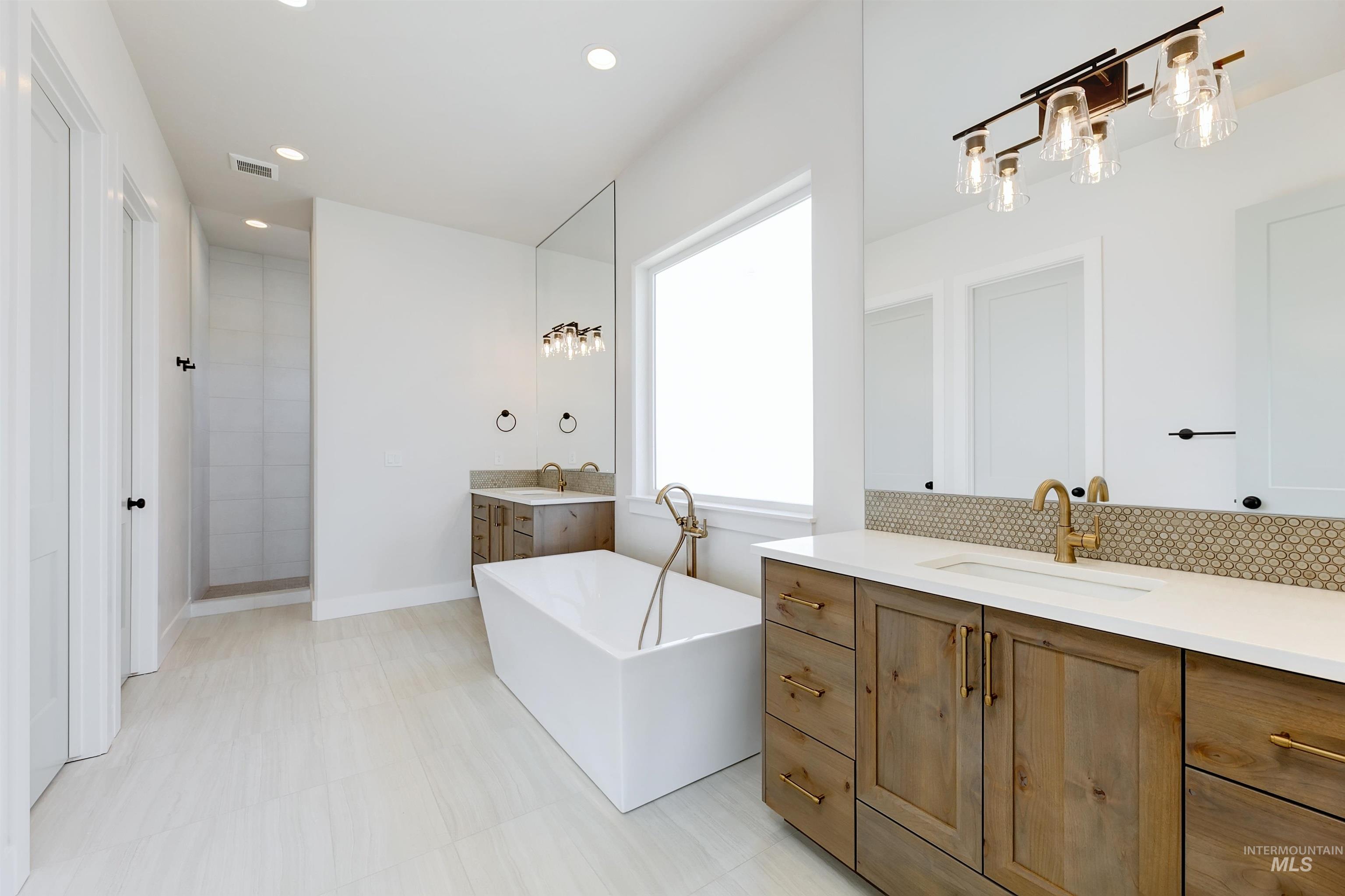 Bathroom featuring a freestanding tub, two vanities, recessed lighting, walk in shower, and backsplash