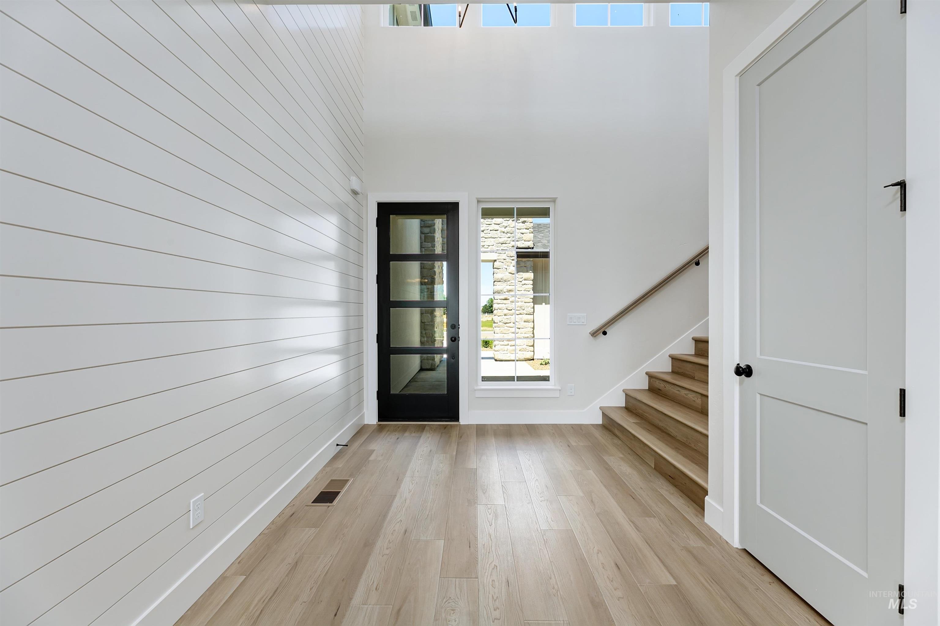 Foyer entrance featuring stairway, light wood-type flooring, wood walls, and a high ceiling