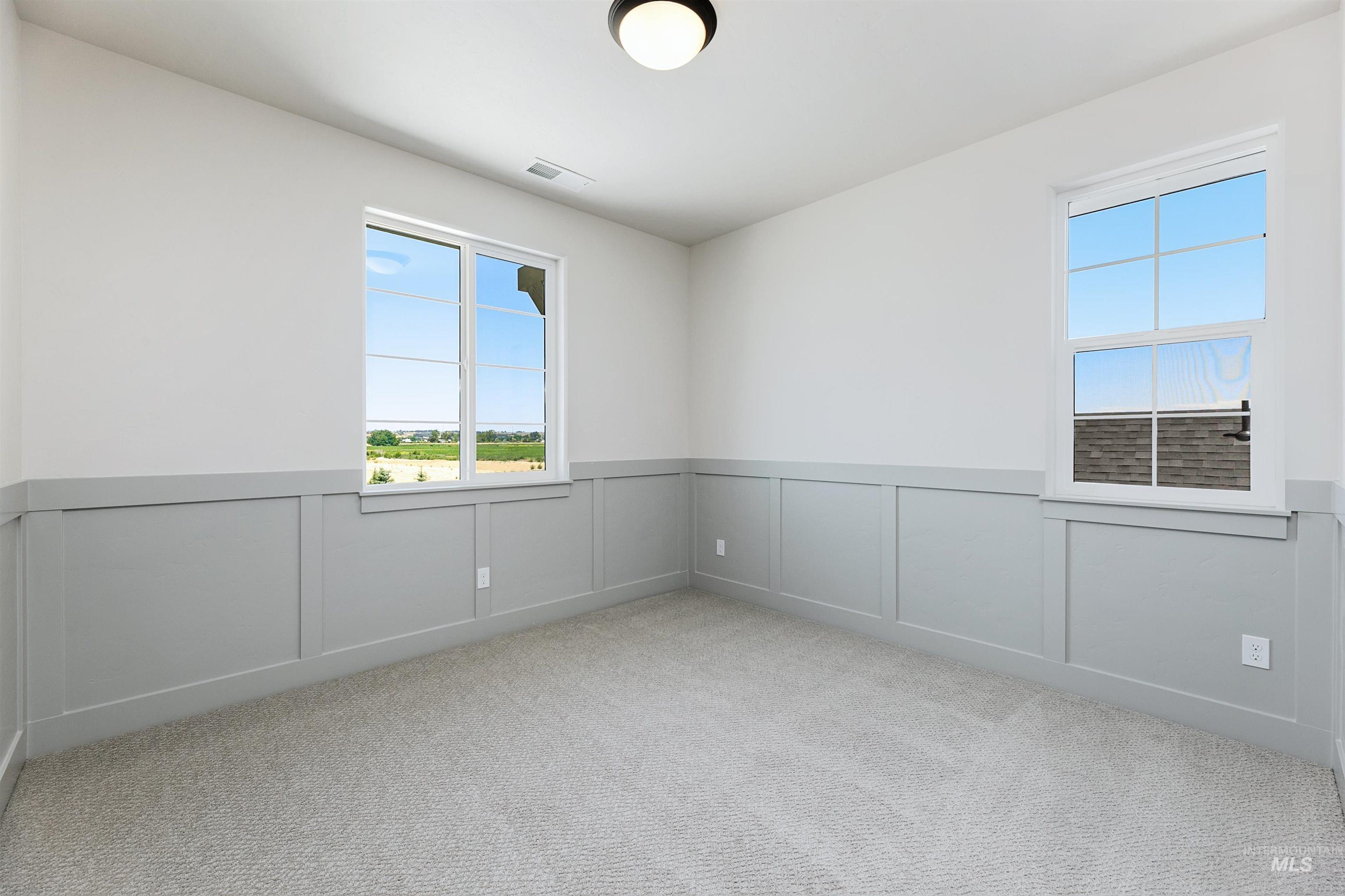 Empty room with a decorative wall, wainscoting, and light carpet