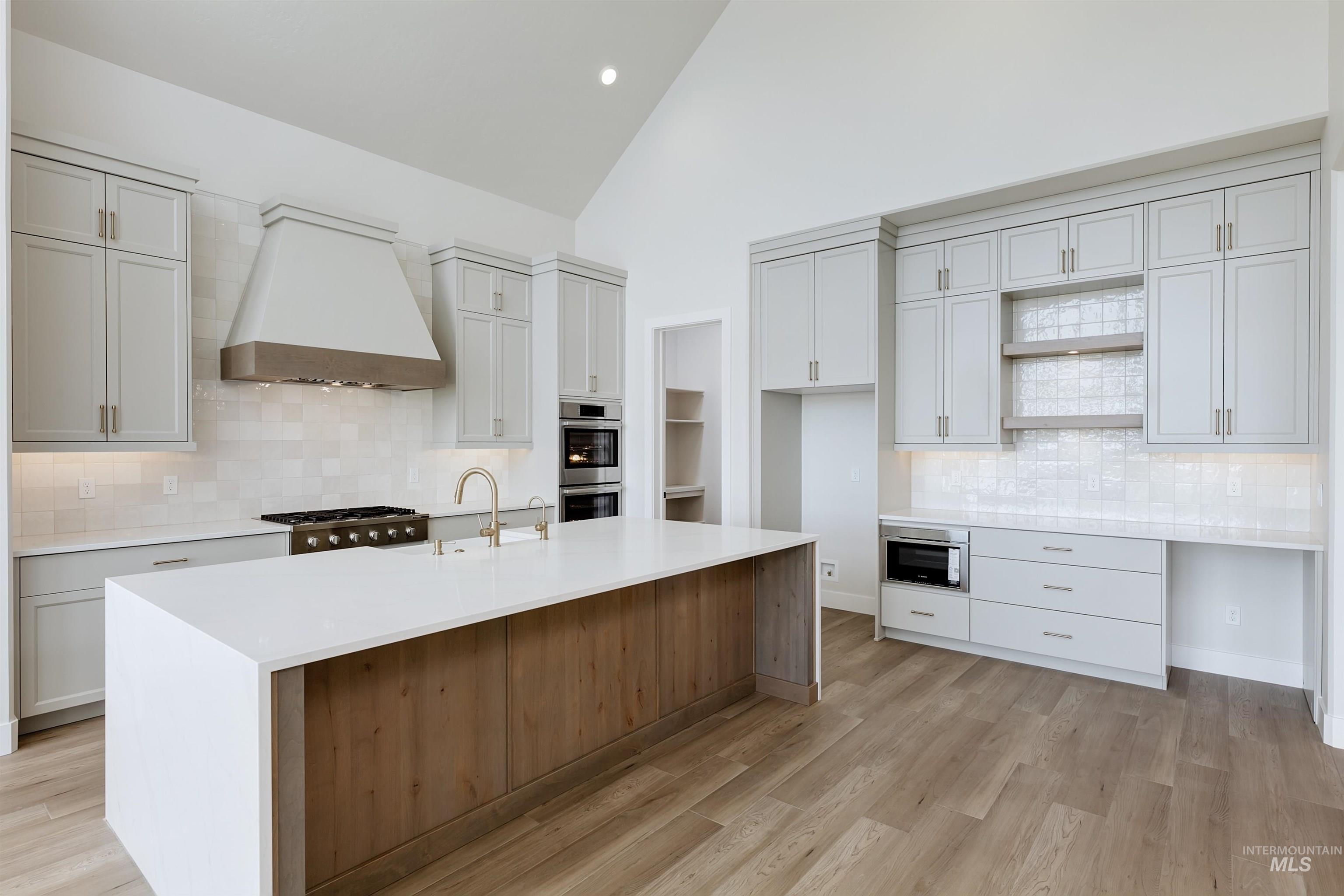 Kitchen featuring backsplash, light stone countertops, high vaulted ceiling, premium range hood, and an island with sink