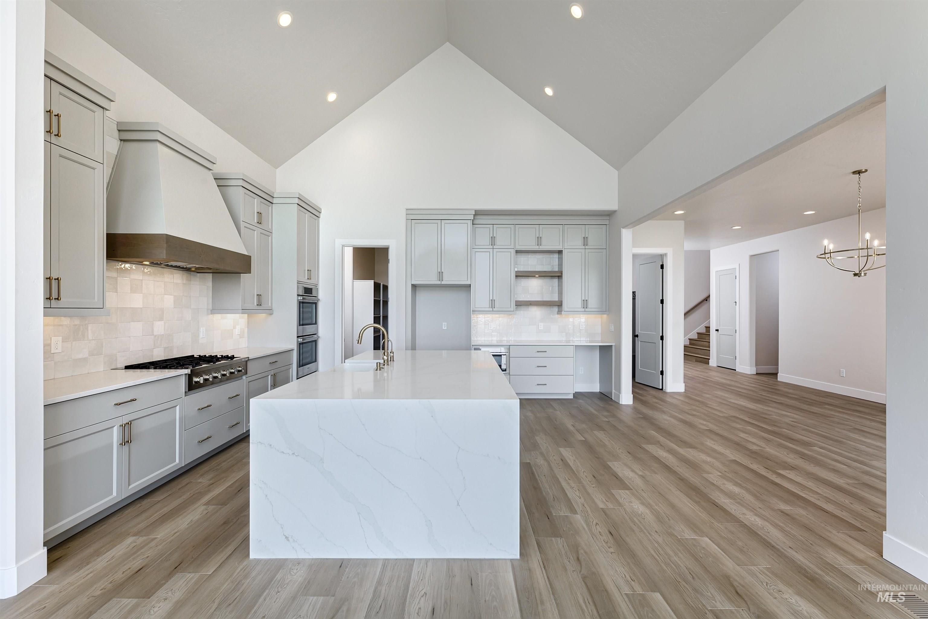 Kitchen featuring a center island with sink, decorative backsplash, light stone counters, custom range hood, and light wood-style floors