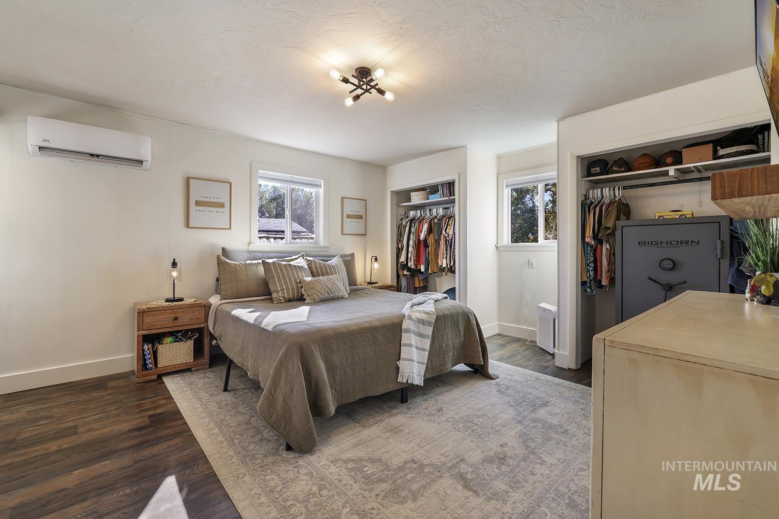 Bedroom with multiple closets, dark wood-style flooring, an AC wall unit, and a textured ceiling