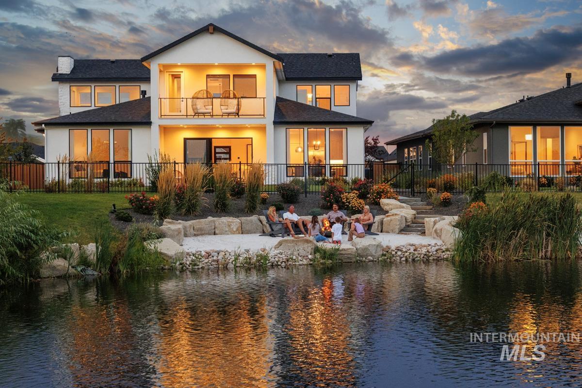 Back of house at dusk featuring a balcony, a patio, roof with shingles, a water view, and stucco siding