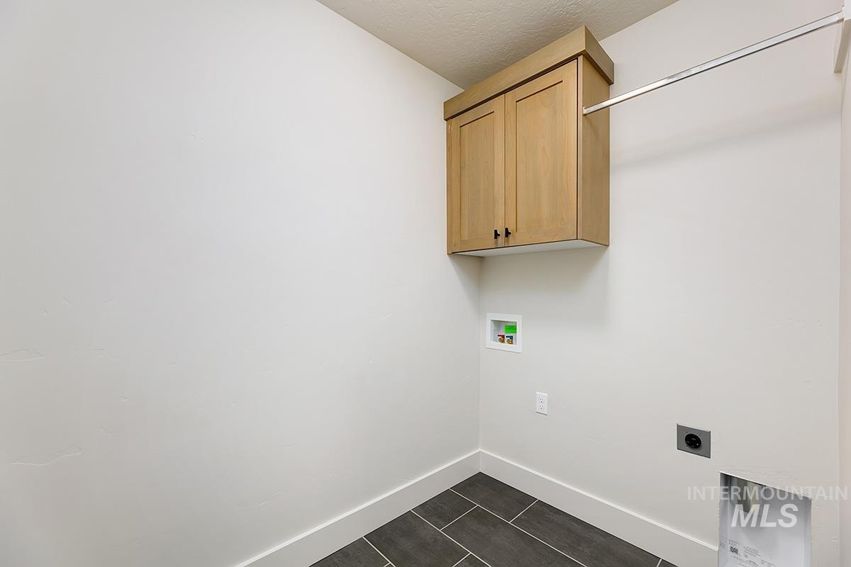 Laundry room featuring electric dryer hookup, hookup for a washing machine, a textured ceiling, cabinet space, and dark tile patterned flooring