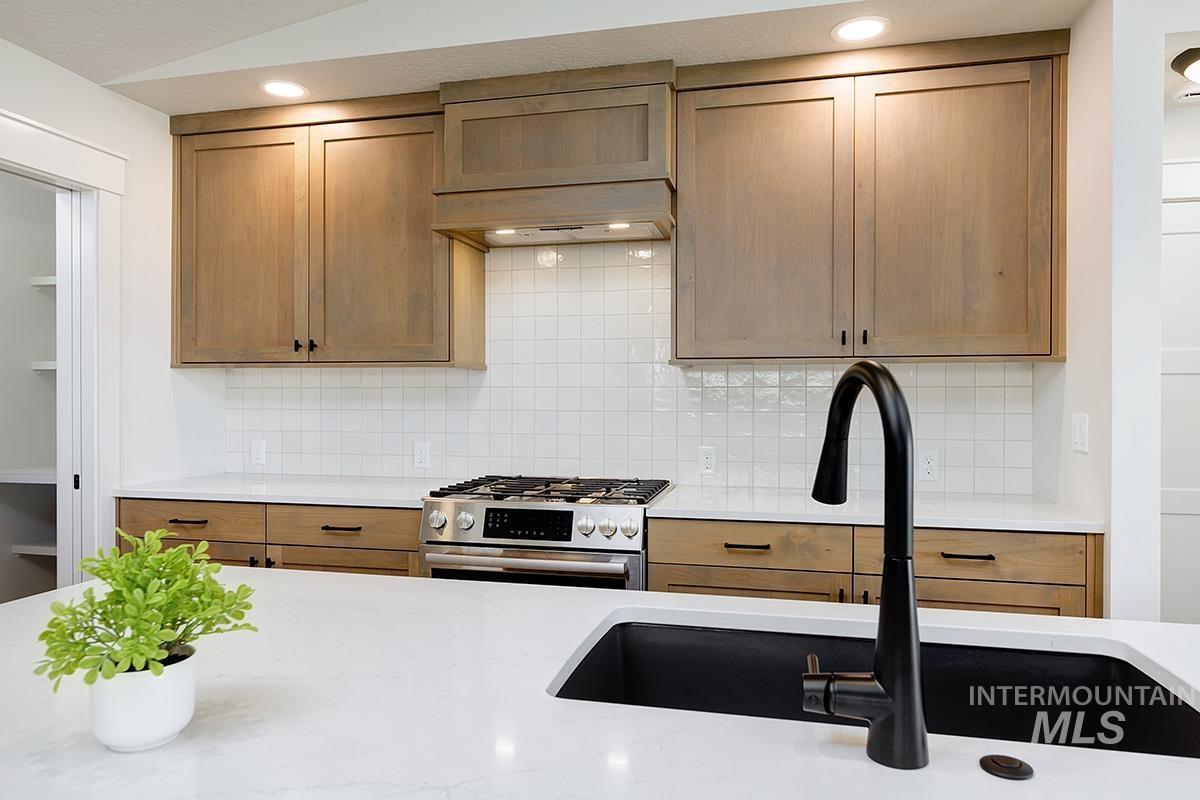 Kitchen with stainless steel range with gas stovetop, backsplash, light stone counters, custom range hood, and brown cabinets