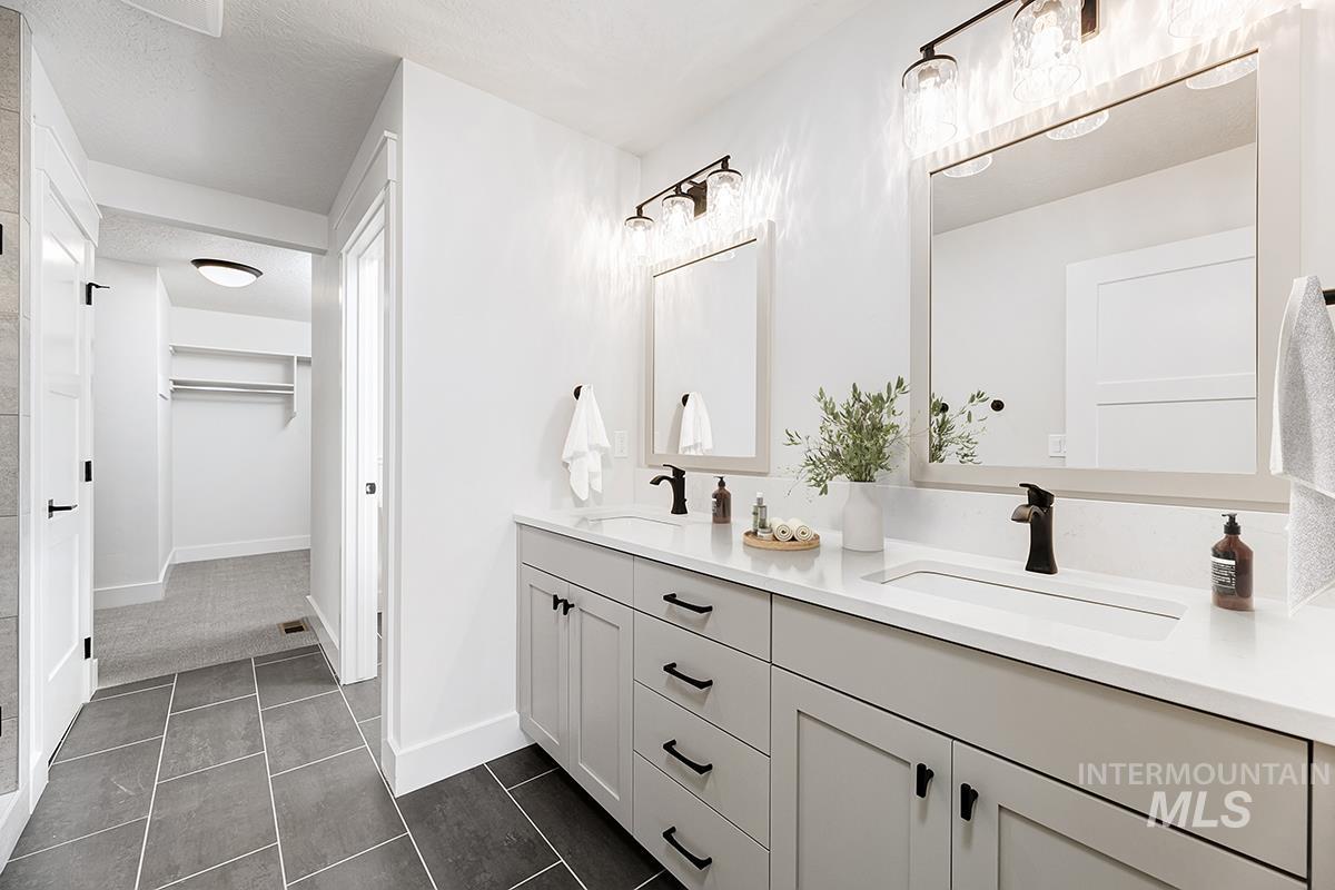 Full bath with double vanity, a spacious closet, a textured ceiling, dark tile patterned floors, and dark colored carpet