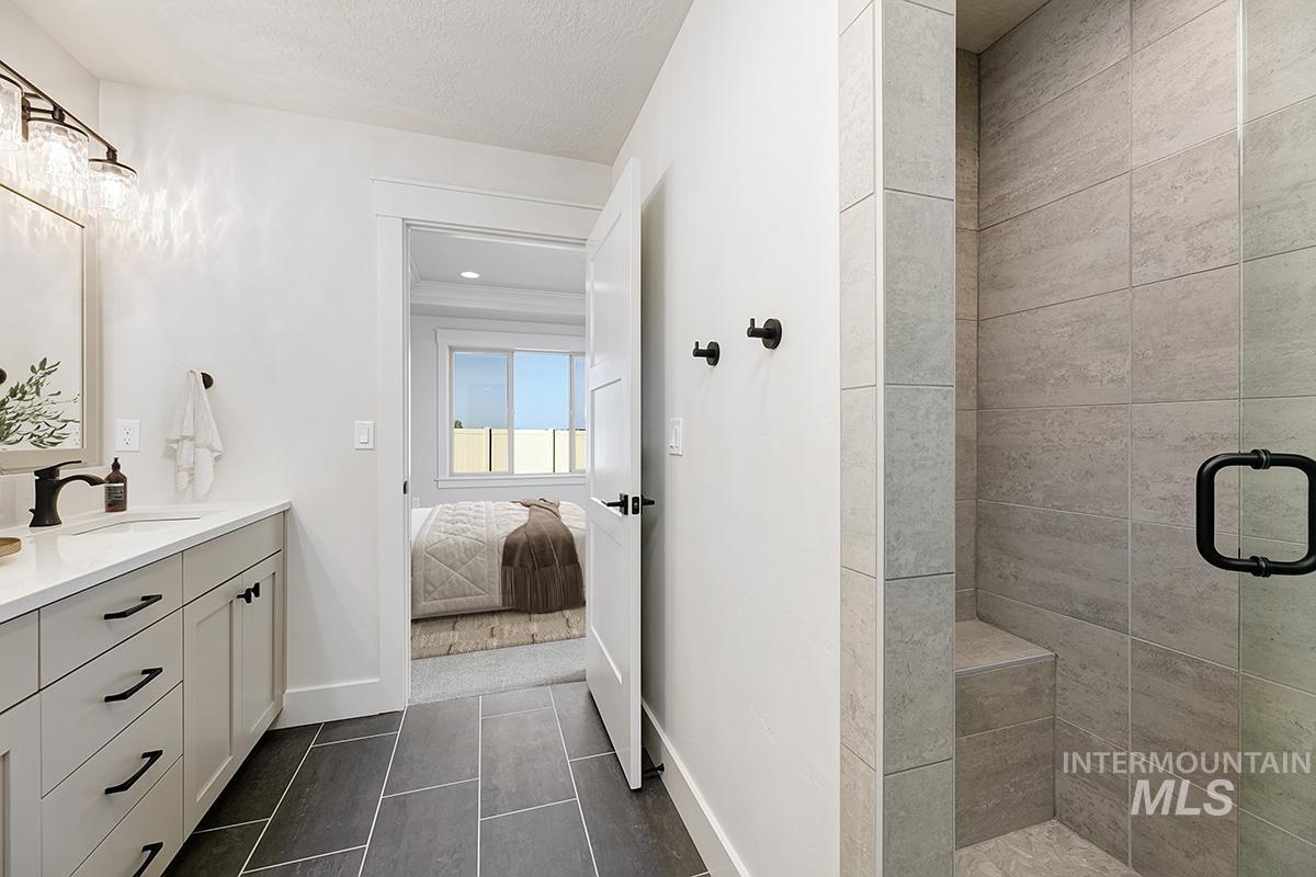Ensuite bathroom with vanity, a shower stall, dark tile patterned floors, and a textured ceiling
