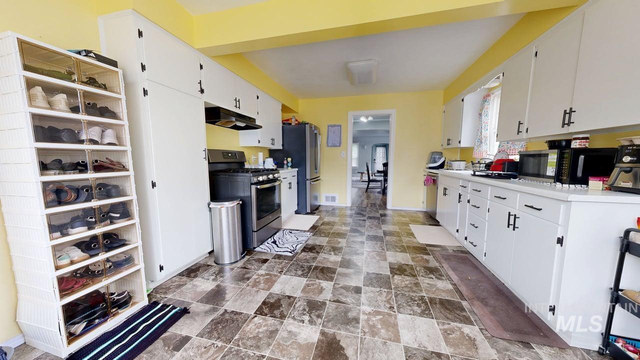 Kitchen with appliances with stainless steel finishes, white cabinetry, and stone finish floors
