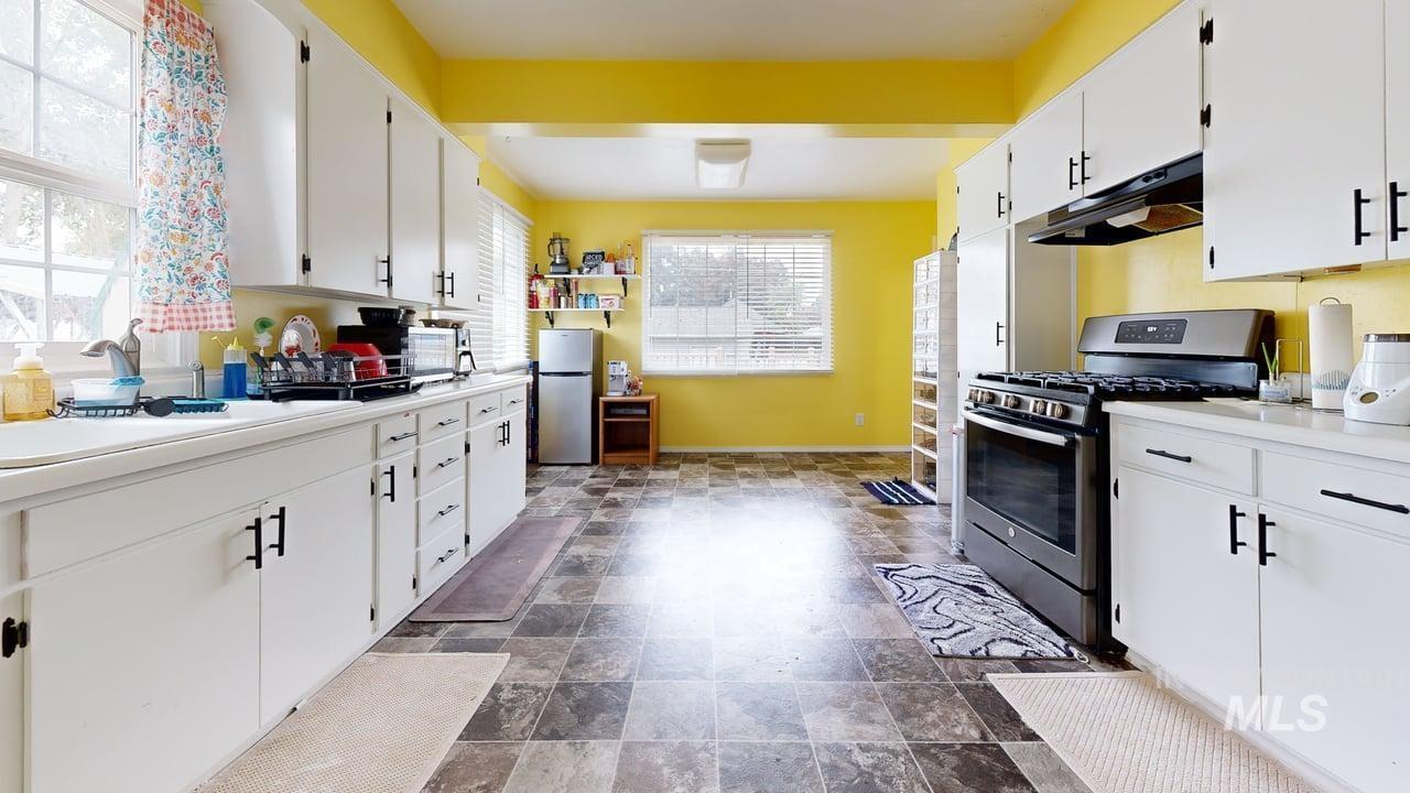 Kitchen featuring stainless steel appliances, white cabinetry, stone finish floors, and under cabinet range hood