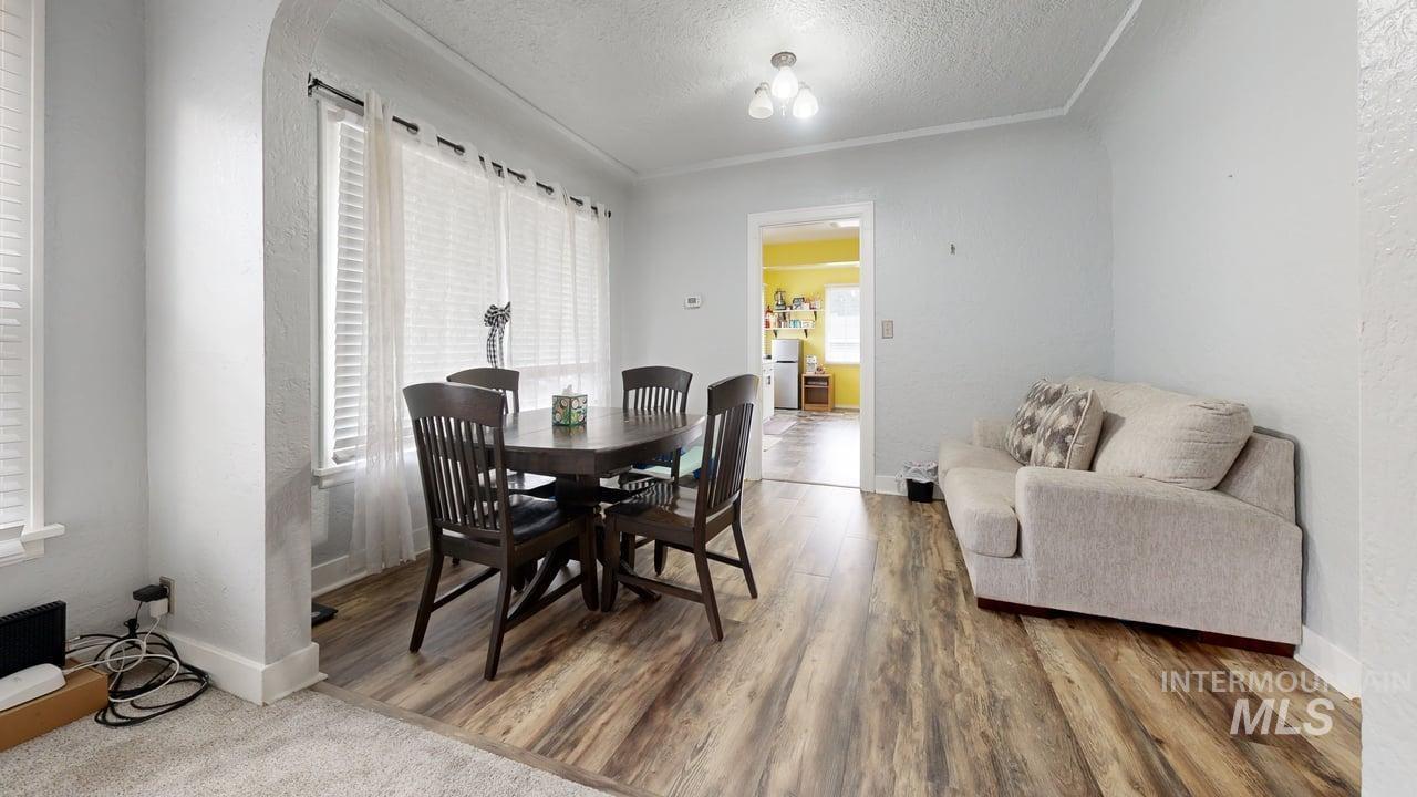 Dining room featuring a textured ceiling, a textured wall, wood finished floors, and crown molding