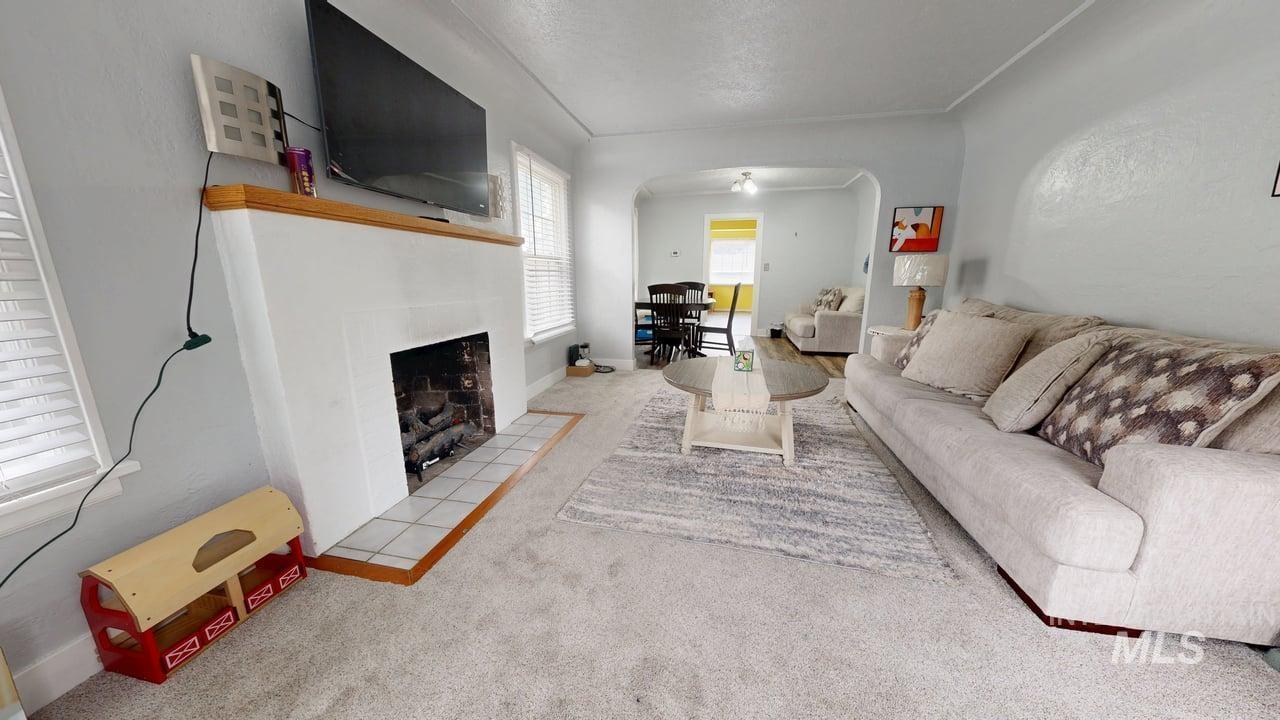 Living room featuring carpet flooring, arched walkways, a tiled fireplace, a textured ceiling, and tile patterned floors