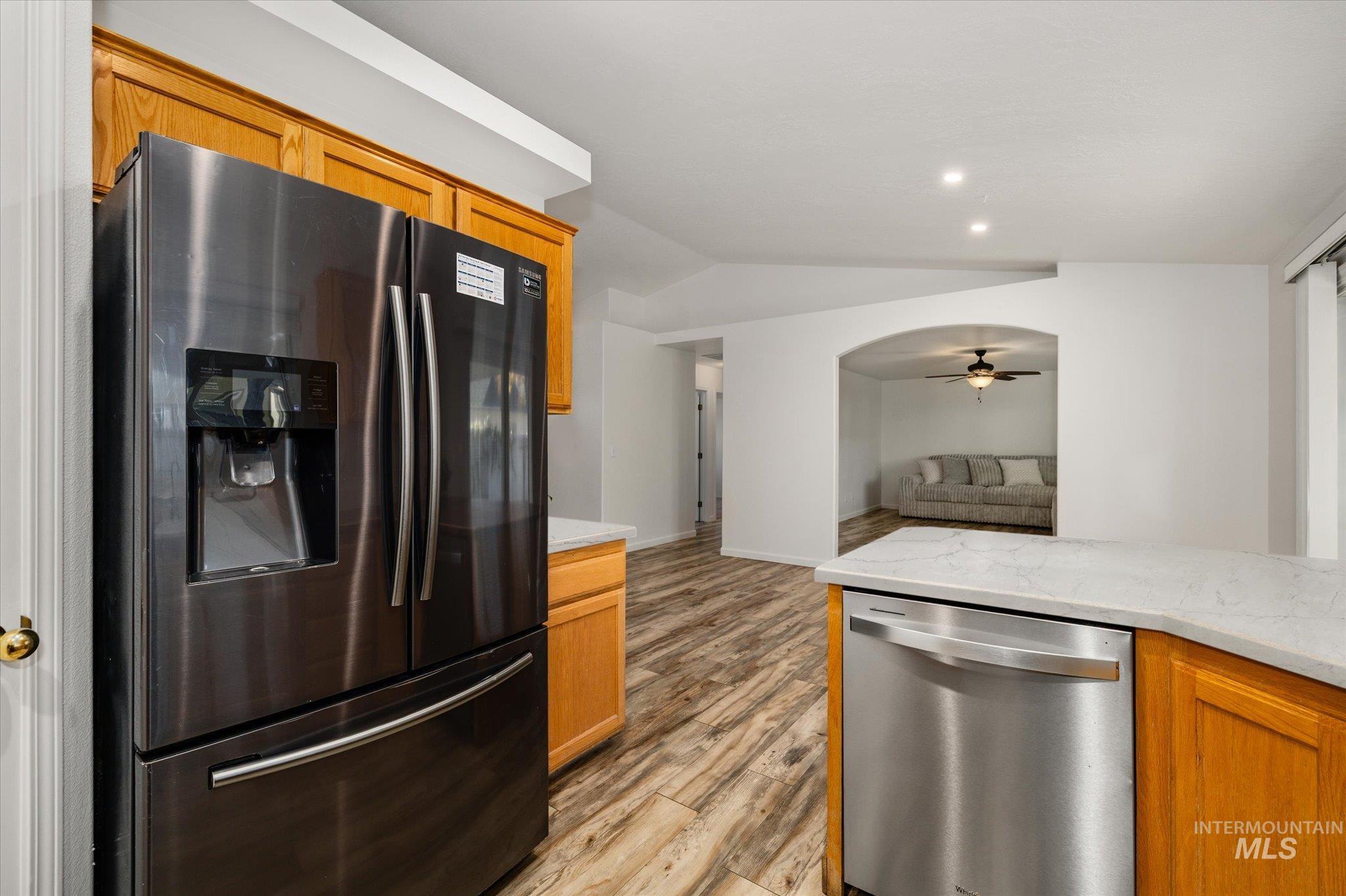 Kitchen featuring appliances with stainless steel finishes, light stone countertops, a ceiling fan, light wood-style floors, and lofted ceiling