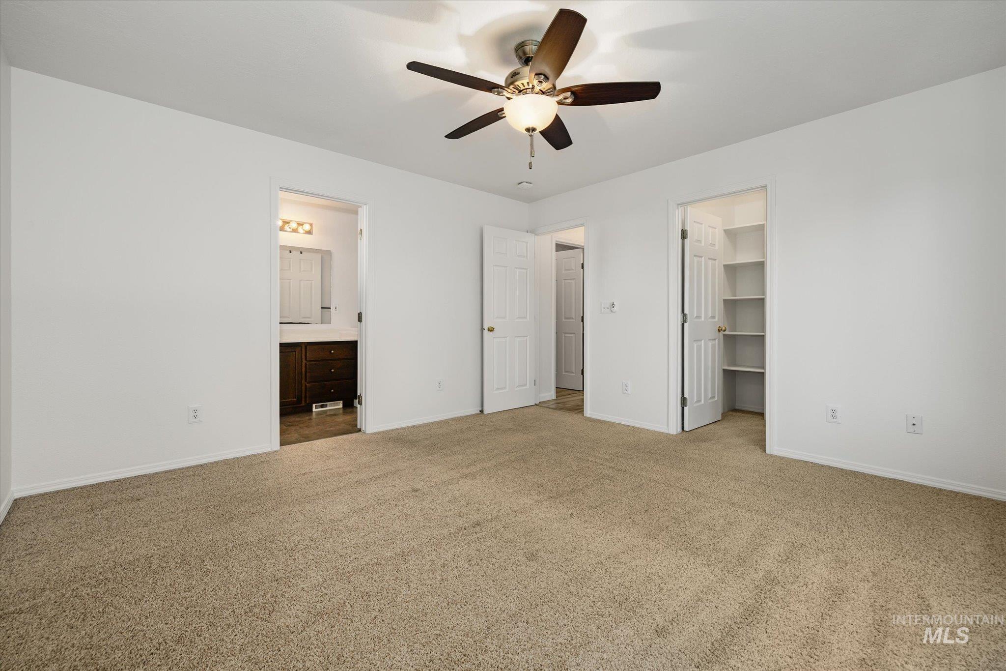 Unfurnished bedroom with light carpet, a walk in closet, a ceiling fan, and ensuite bath