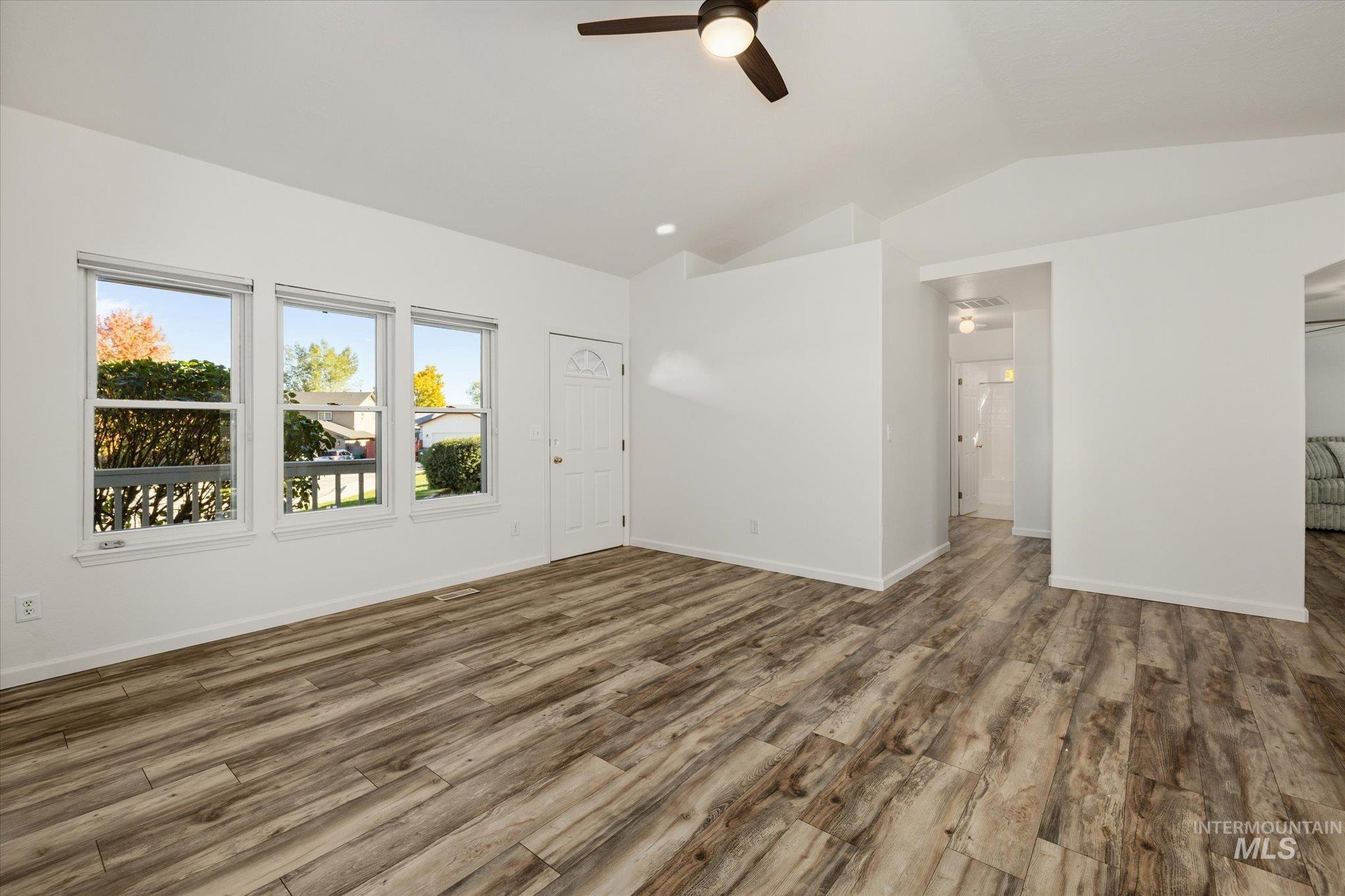 Unfurnished living room with vaulted ceiling, wood finished floors, and a ceiling fan
