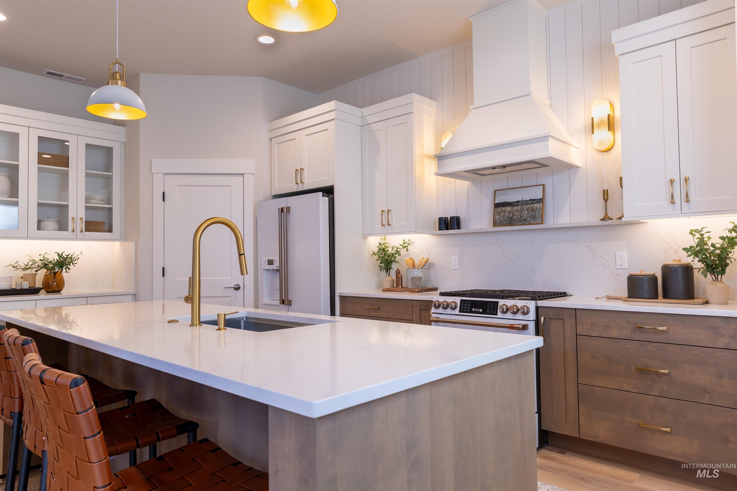 Kitchen featuring white cabinetry, custom range hood, pendant lighting, premium appliances, and an island with sink