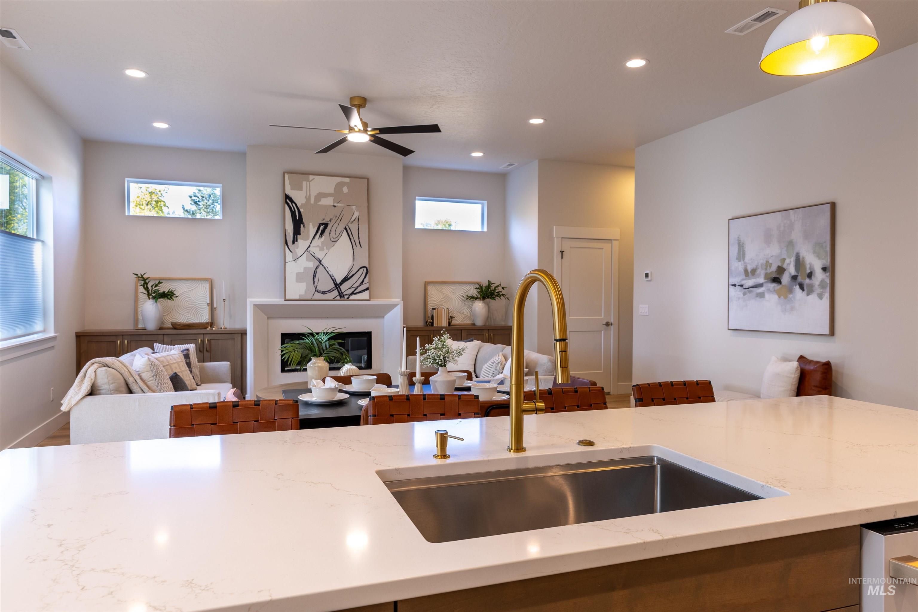 Kitchen with open floor plan, a glass covered fireplace, light stone countertops, recessed lighting, and a ceiling fan