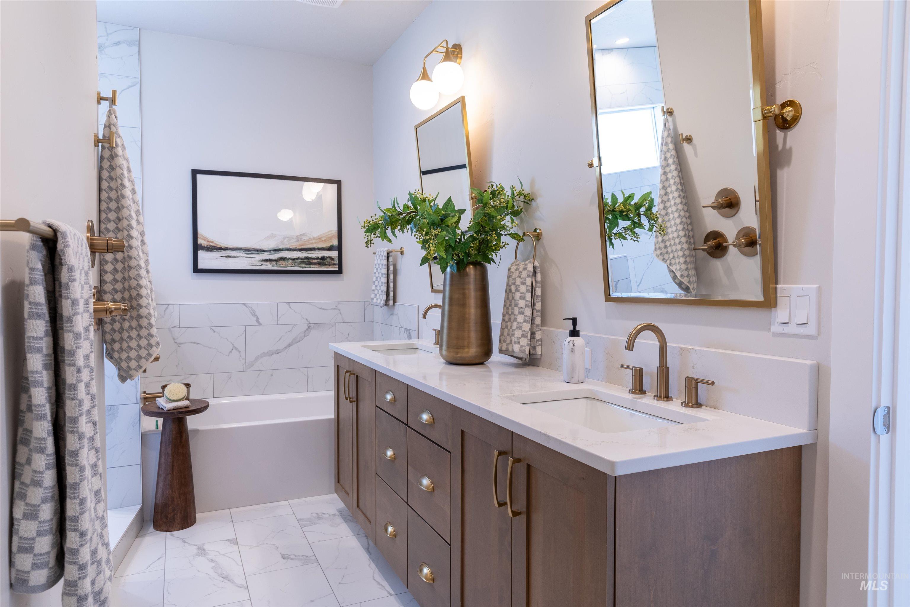 Full bathroom with light marble finish floors, double vanity, tile walls, and a shower