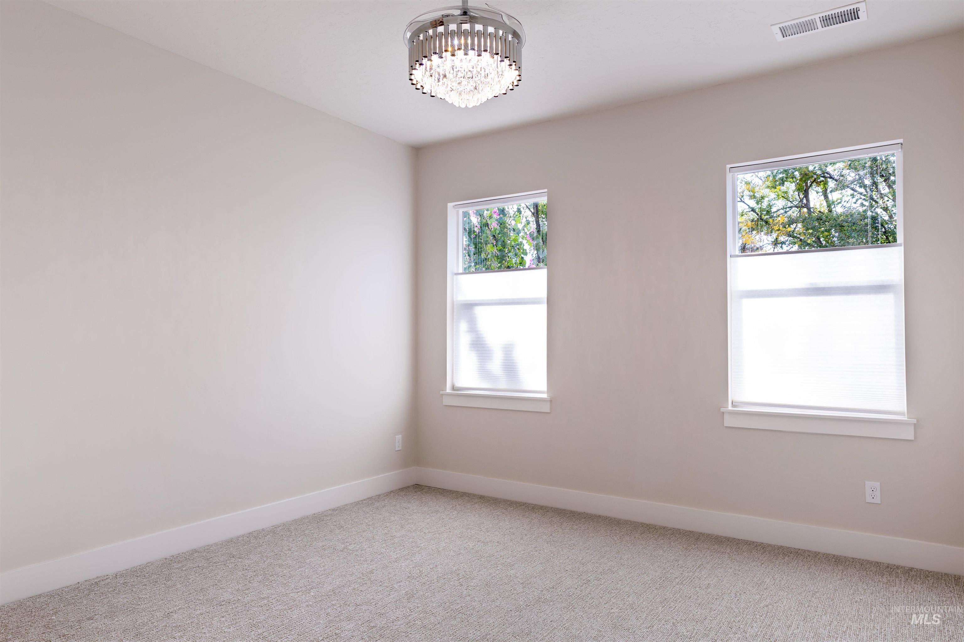 Carpeted empty room featuring baseboards and a chandelier