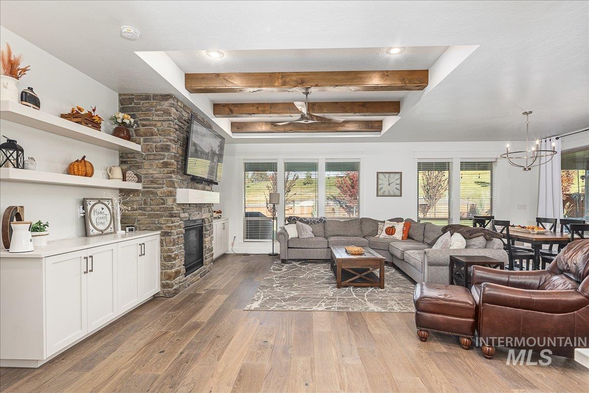 Living area with beam ceiling, wood finished floors, a stone fireplace, a chandelier, and healthy amount of natural light