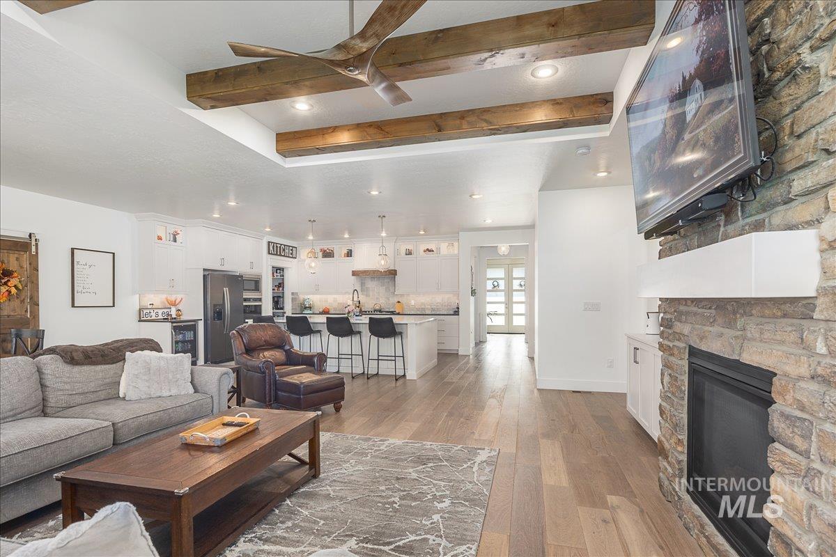 Living room with beam ceiling, light wood-style floors, a stone fireplace, recessed lighting, and beverage cooler