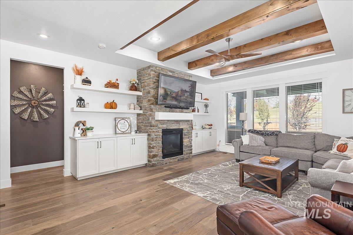 Living room with beam ceiling, light wood finished floors, a fireplace, and a ceiling fan