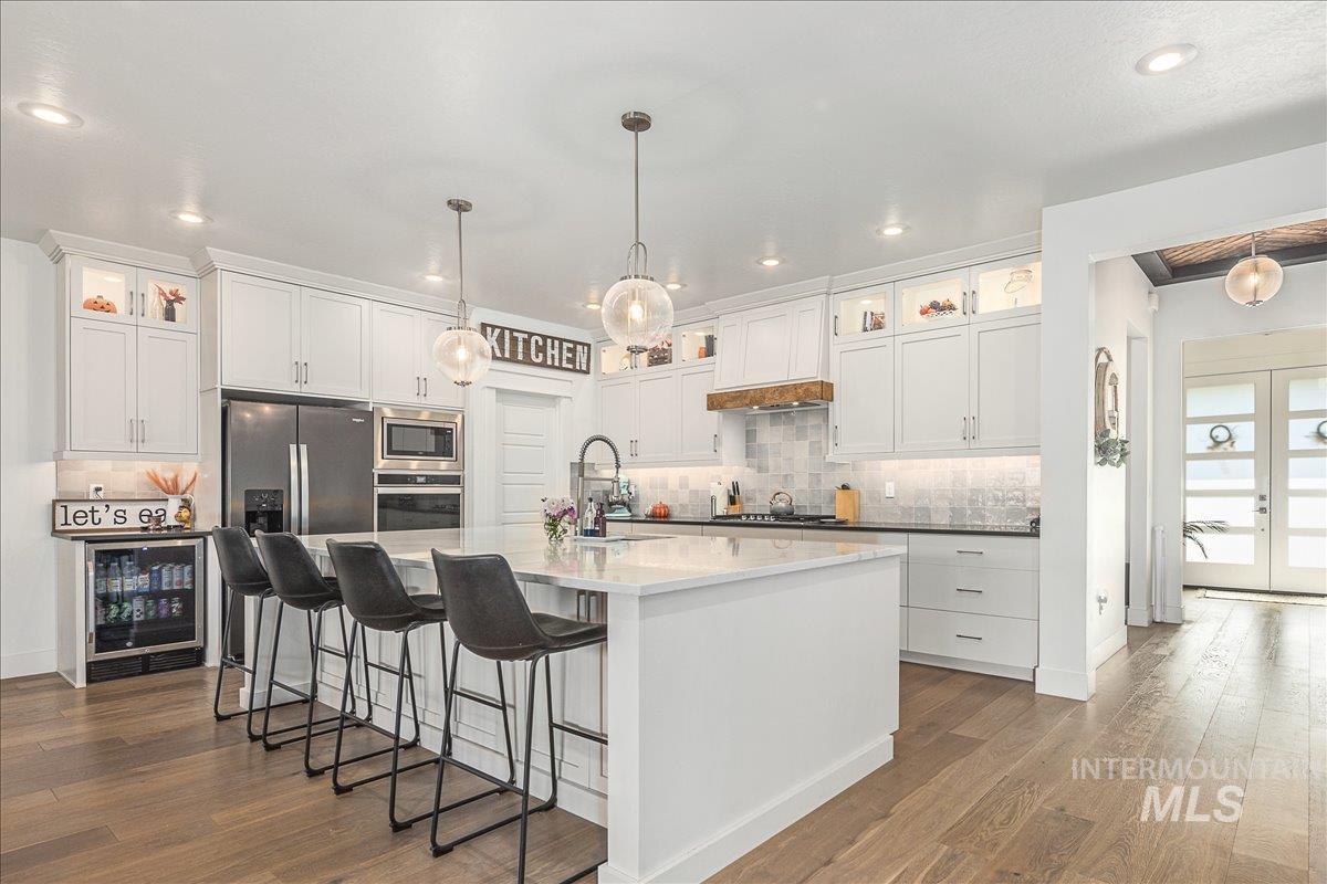 Kitchen featuring glass insert cabinets, white cabinets, a breakfast bar, wine cooler, and backsplash