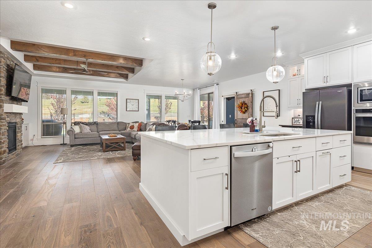 Kitchen featuring white cabinets, open floor plan, light wood finished floors, beam ceiling, and stainless steel appliances