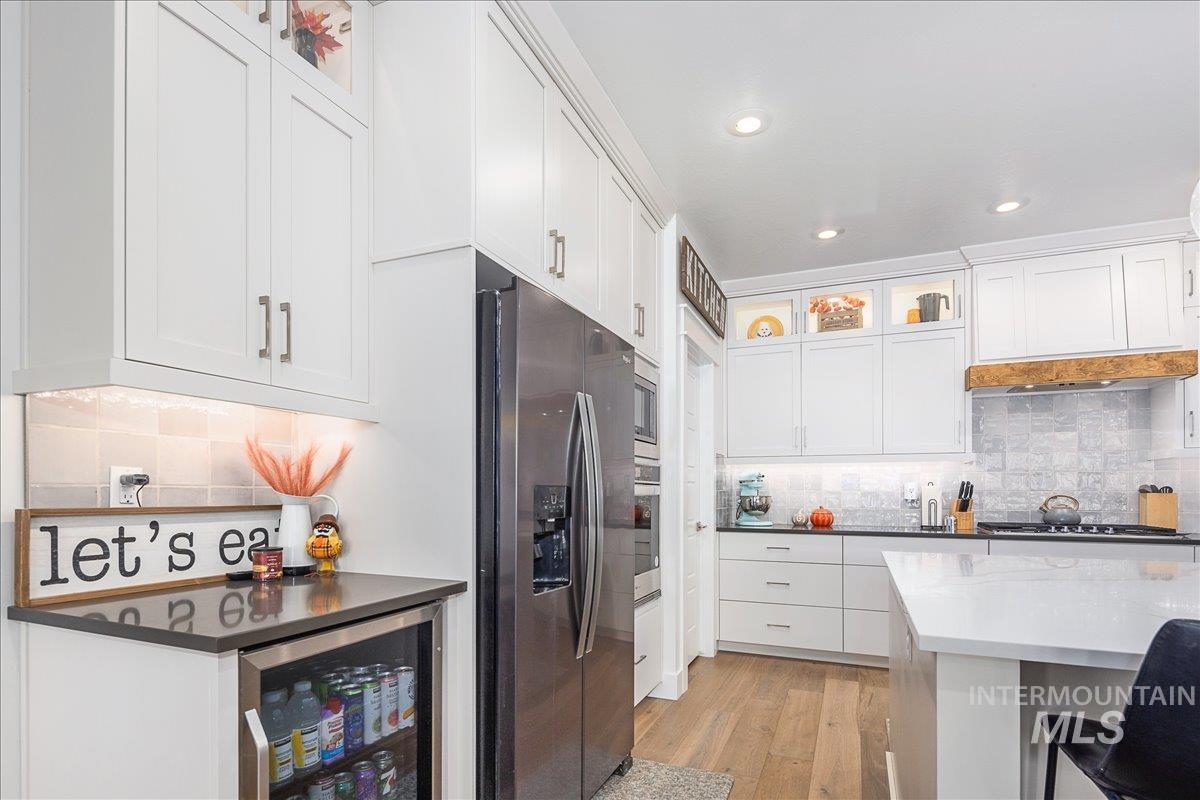 Kitchen with backsplash, white cabinets, appliances with stainless steel finishes, wine cooler, and recessed lighting