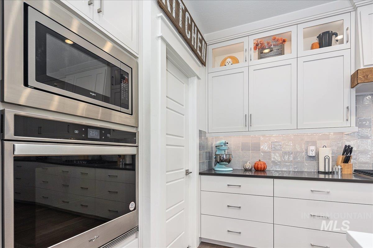 Kitchen featuring appliances with stainless steel finishes, white cabinets, backsplash, and glass insert cabinets