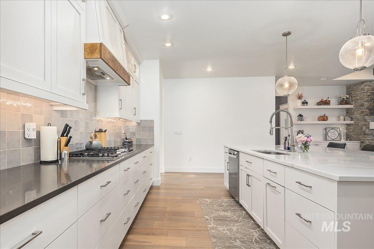 Kitchen with white cabinets, light wood-style floors, hanging light fixtures, dark stone counters, and recessed lighting