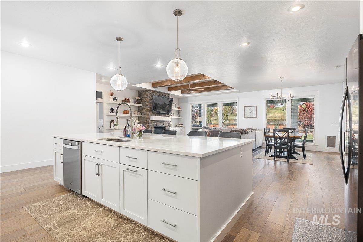 Kitchen featuring white cabinets, a stone fireplace, light wood-style floors, a center island with sink, and open floor plan