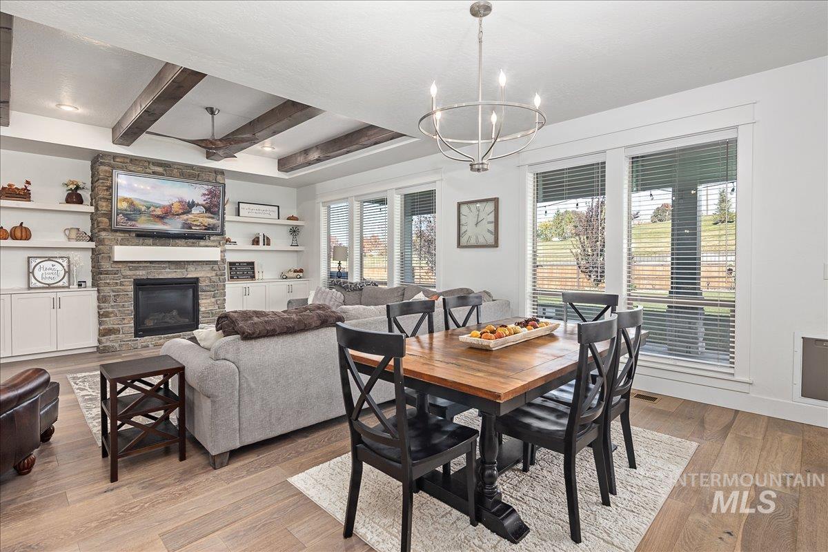 Dining space with a fireplace, beam ceiling, light wood-type flooring, a chandelier, and ceiling fan