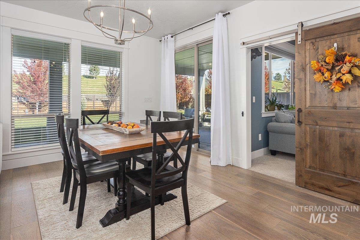 Dining area with wood finished floors, a barn door, and a chandelier