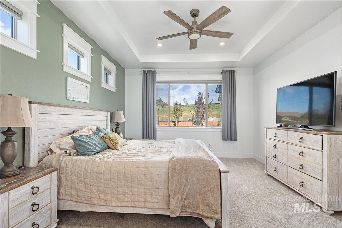 Carpeted bedroom with a raised ceiling, ceiling fan, and recessed lighting