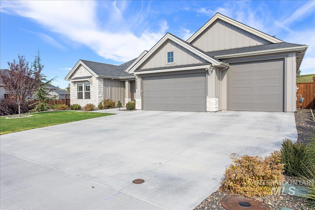 View of front of property with board and batten siding, driveway, an attached garage, stone siding, and a shingled roof