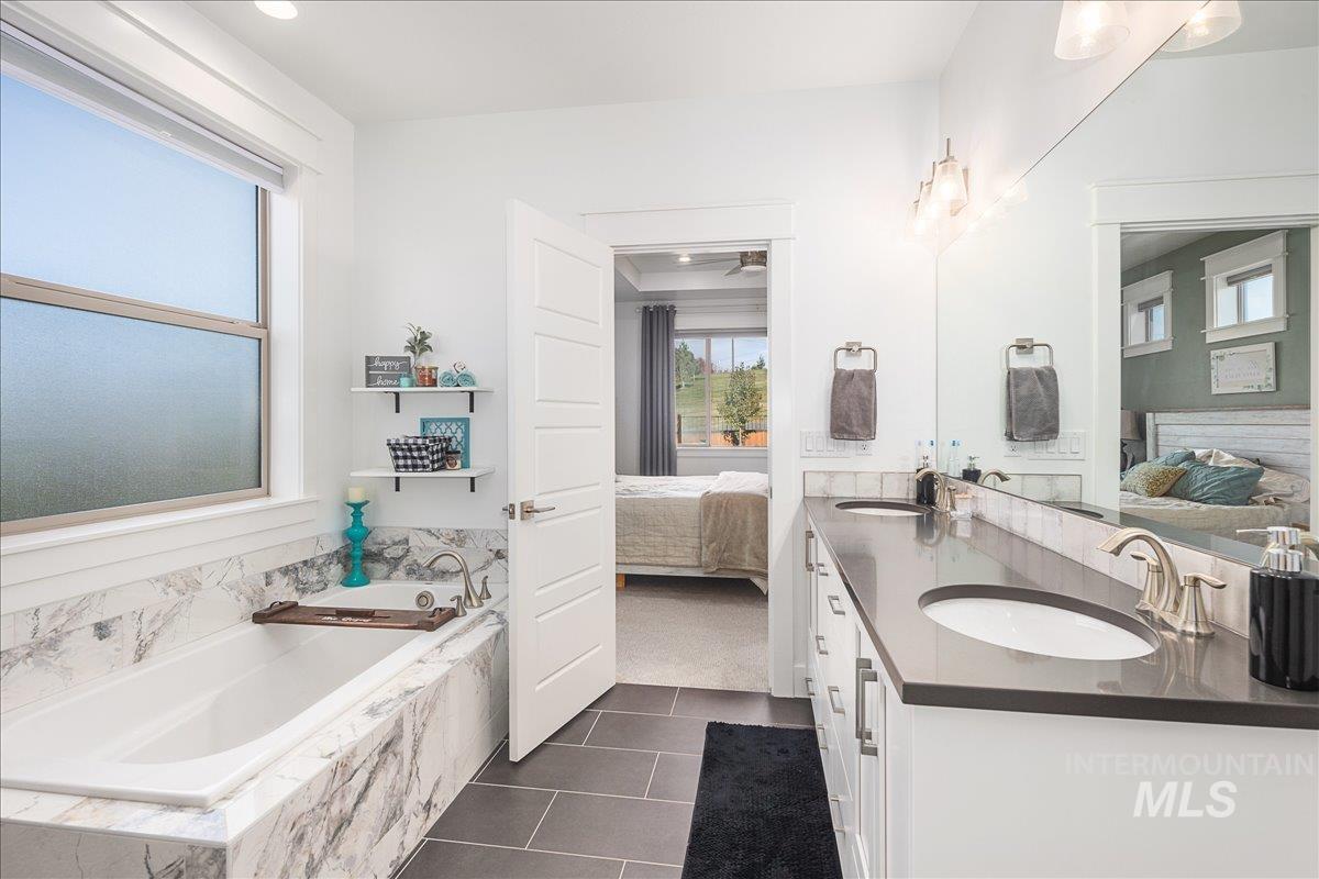 Ensuite bathroom featuring double vanity, a garden tub, dark tile patterned floors, and dark colored carpet