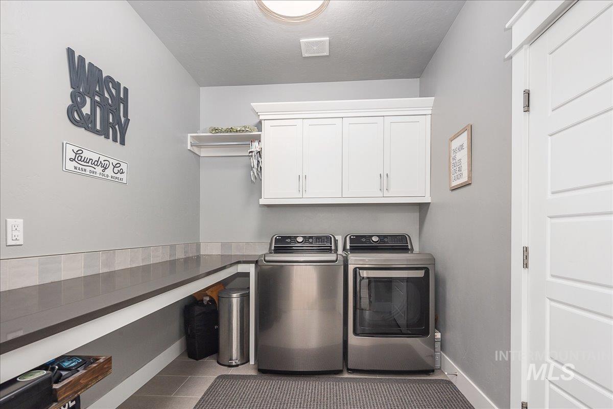 Laundry area featuring independent washer and dryer, a textured ceiling, light tile patterned floors, and cabinet space