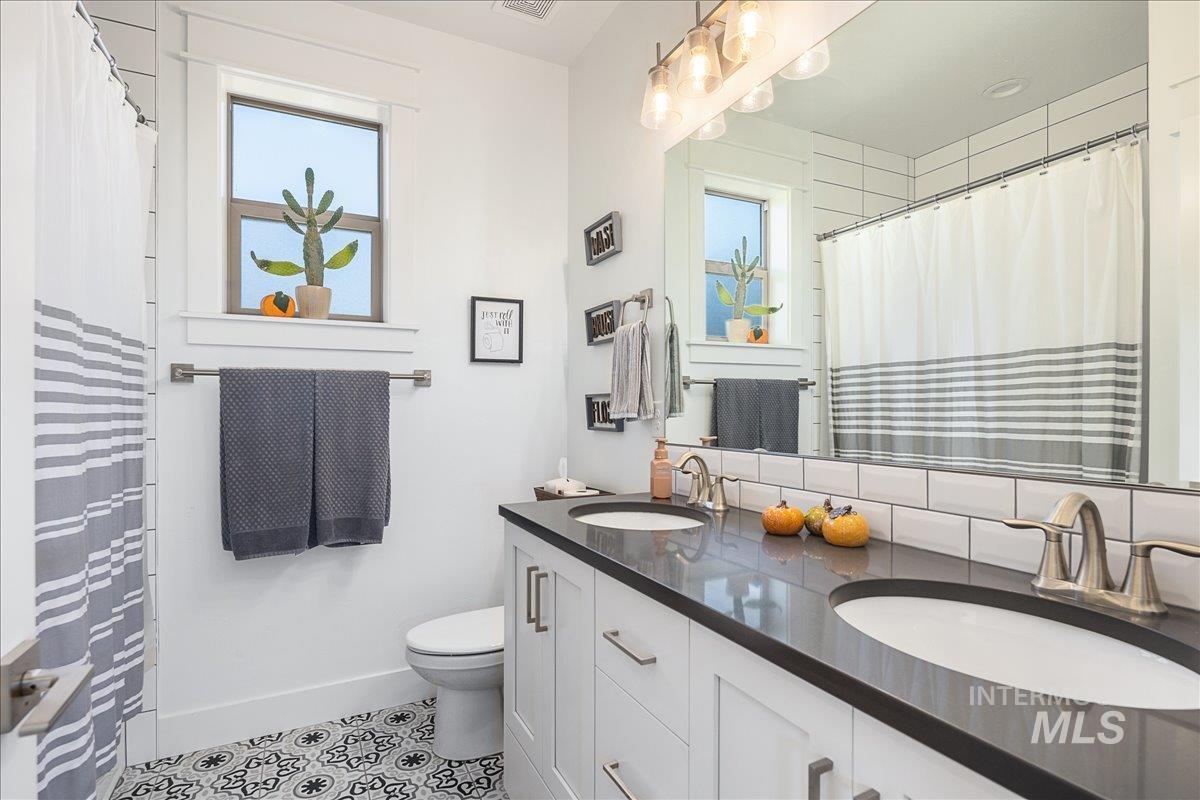 Bathroom featuring double vanity, curtained shower, decorative backsplash, and light tile patterned floors