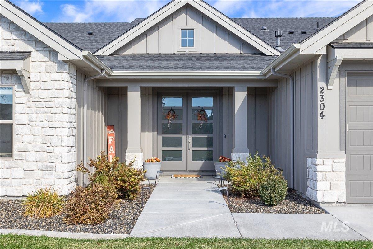 Property entrance with board and batten siding, stone siding, roof with shingles, and french doors