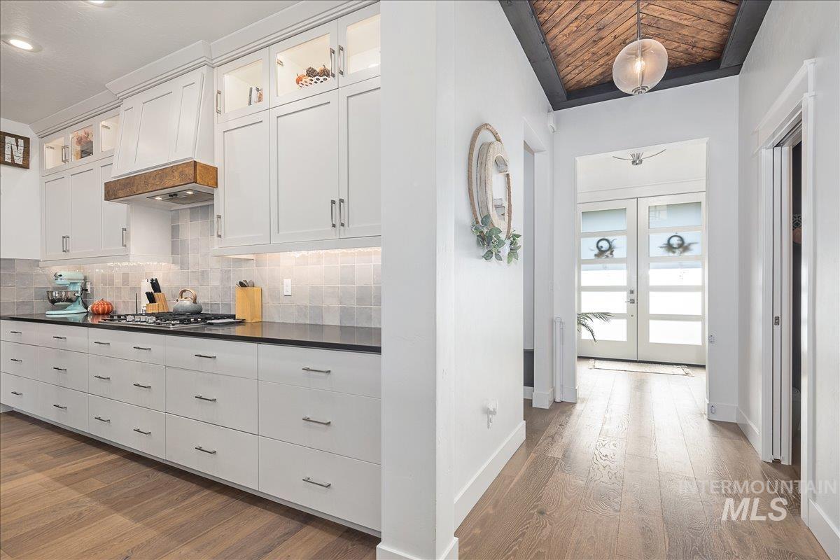 Kitchen featuring glass insert cabinets, dark wood-style flooring, decorative backsplash, white cabinets, and wood ceiling