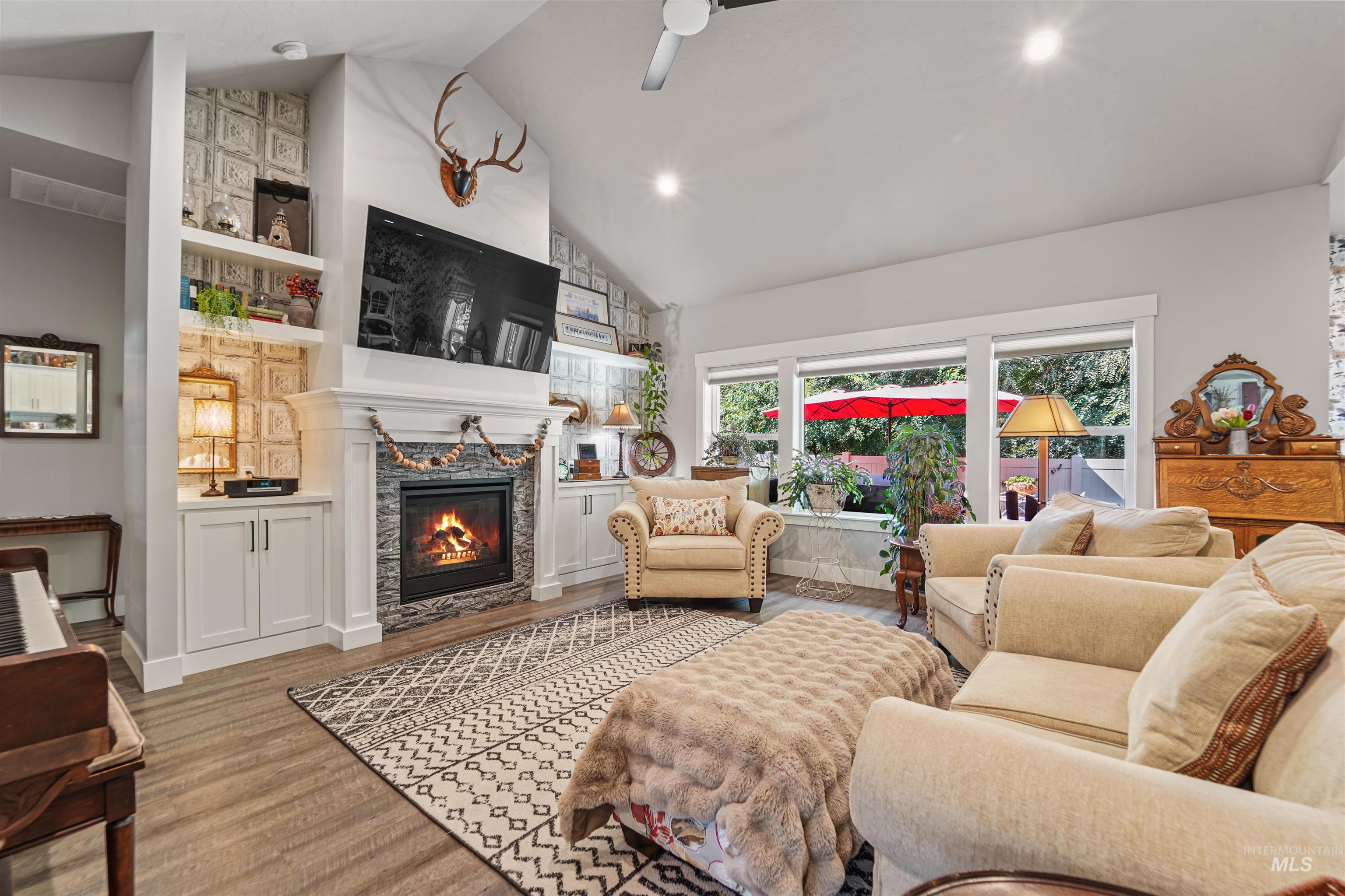 Living room with a fireplace, high vaulted ceiling, wood finished floors, ceiling fan, and built in shelves