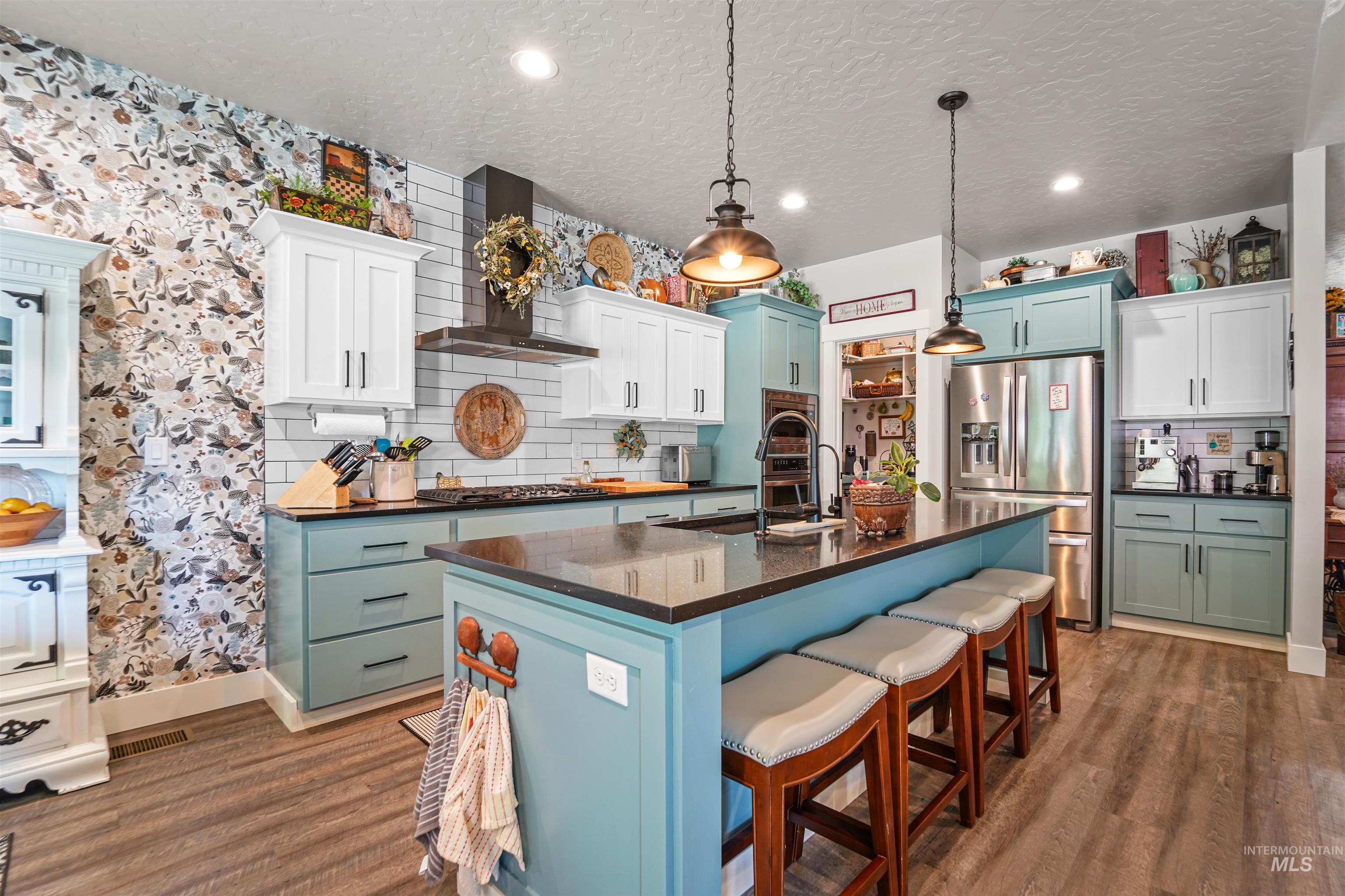 Kitchen with tasteful backsplash, decorative light fixtures, a center island with sink, a breakfast bar area, and wall chimney exhaust hood